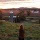 Woman looking out over farm field at sunset